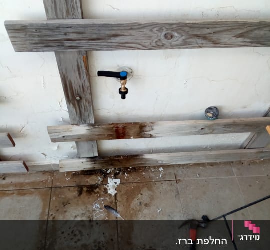 ברז מים על קיר עץ עם כלים על הרצפה